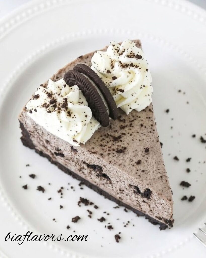 No Bake Oreo Cheesecake with creamy filling, Oreo cookie crust, and whipped cream topping decorated with Oreo halves and crumbs on a serving plate.