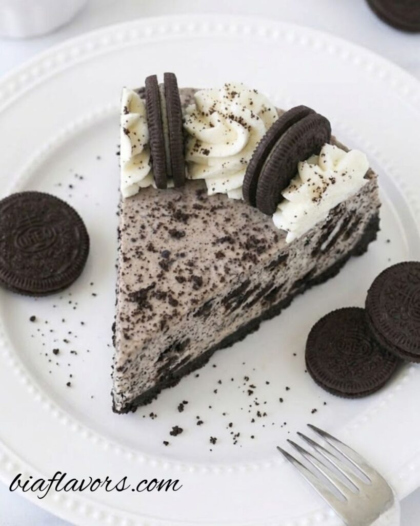 No Bake Oreo Cheesecake with creamy filling, Oreo cookie crust, and whipped cream topping decorated with Oreo halves and crumbs on a serving plate.