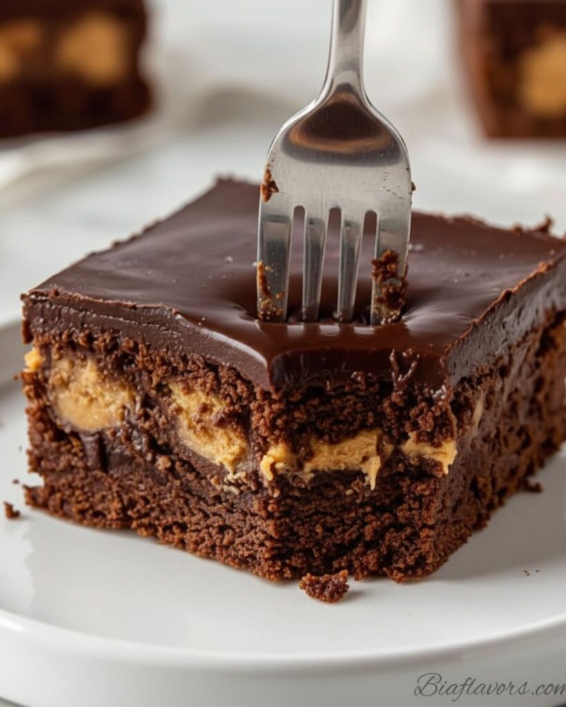 Silver fork cutting into peanut butter stuffed brownie on white plate showing fudgy dark interior with golden peanut butter chunk and ganache on top