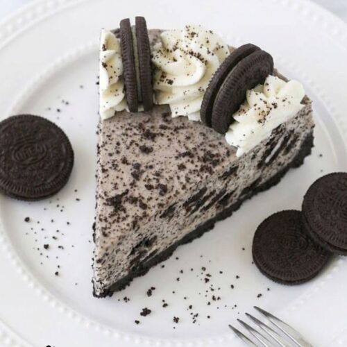 No Bake Oreo Cheesecake with creamy filling, Oreo cookie crust, and whipped cream topping decorated with Oreo halves and crumbs on a serving plate.