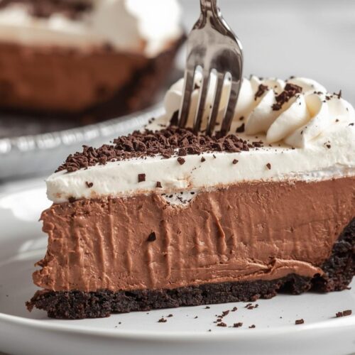 Rich chocolate cream pie with Oreo crust and whipped cream topping on a white plate