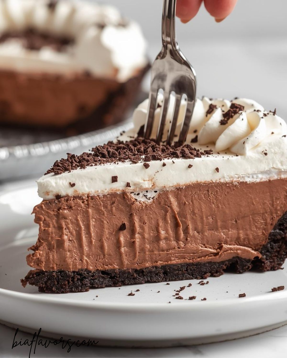 Rich chocolate cream pie with Oreo crust and whipped cream topping on a white plate