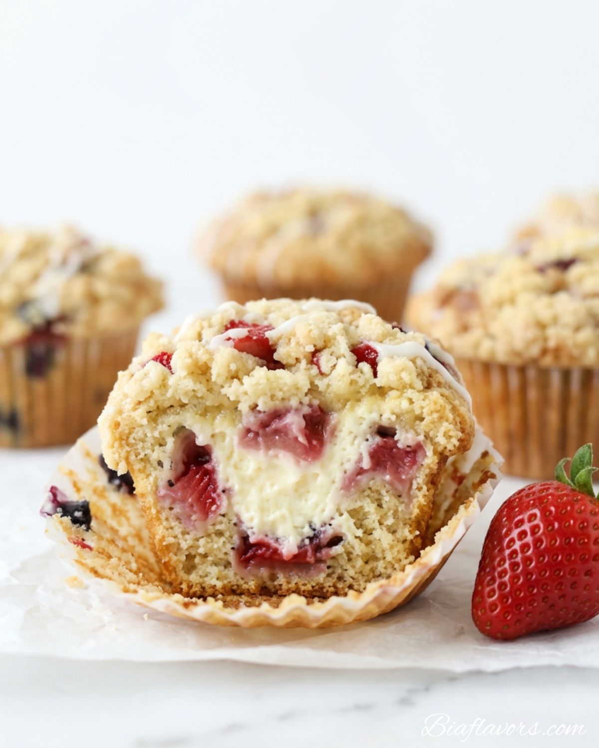 Dramatic close-up of strawberry cheesecake streusel muffin with wrapper peeled showing creamy cheesecake filling strawberry chunks golden streusel and white glaze drizzle